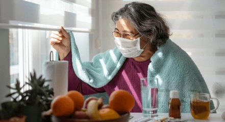 Woman with long COVID wearing a mask, looking out of the window.